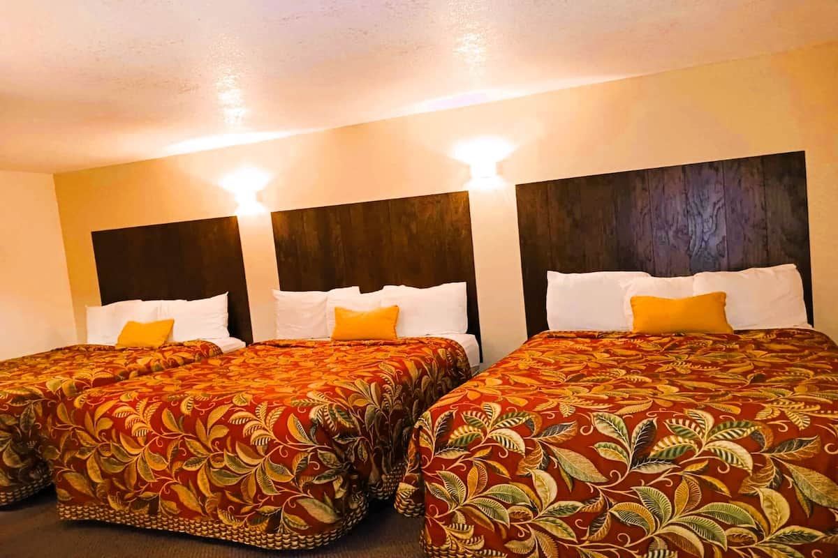 A hotel room with three beds, each with a red floral bedspread and white pillows.