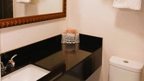 A bathroom with a black countertop sink, a white toilet, and a mirror with a decorative frame. There are shelves with towels and toiletries. - HomeTown Inn By OYO Lakin, KS (Lakin)