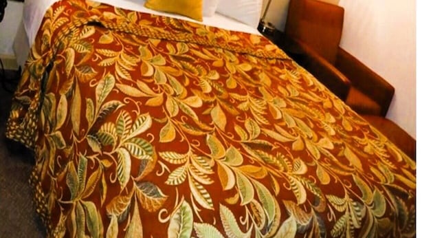 A hotel room with a large bed, a wooden headboard, white bedding, a yellow accent pillow, and a nightstand with a lamp. - HomeTown Inn By OYO Lakin, KS (Lakin)