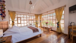 A spacious bedroom with a large bed, wooden floor, and multiple windows with curtains. - Inkarri Cusco (Cusco)