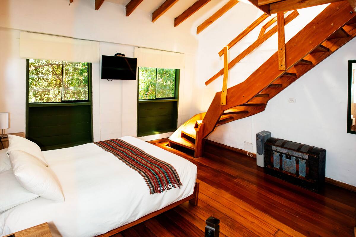 A bedroom with a bed, a wooden staircase, and a fireplace.