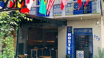 A hostel with multiple flags, a sign reading "ROOMS", and a reception desk with a number "173".