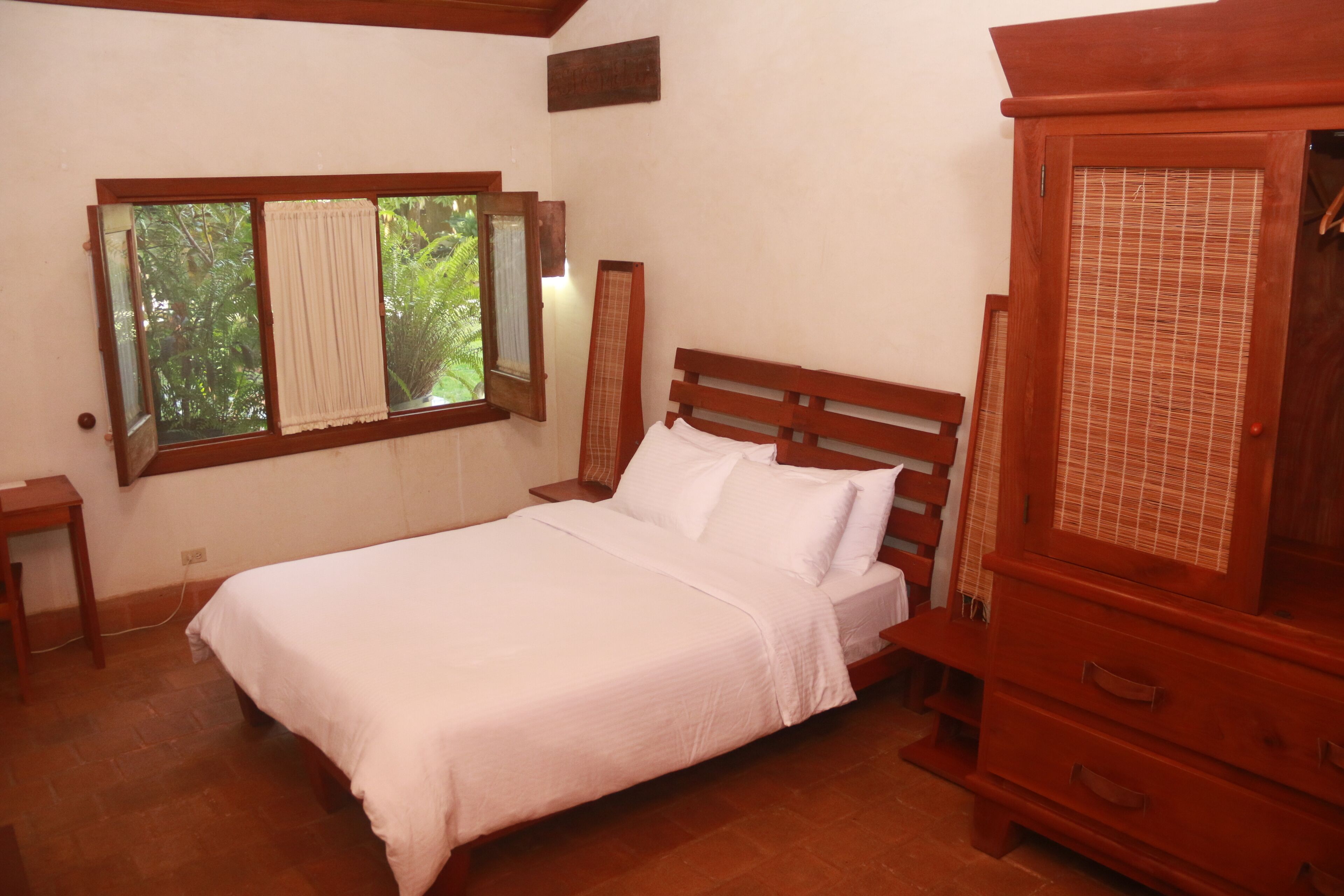 A bedroom with a wooden bed, a nightstand, a dresser, and a window with curtains.