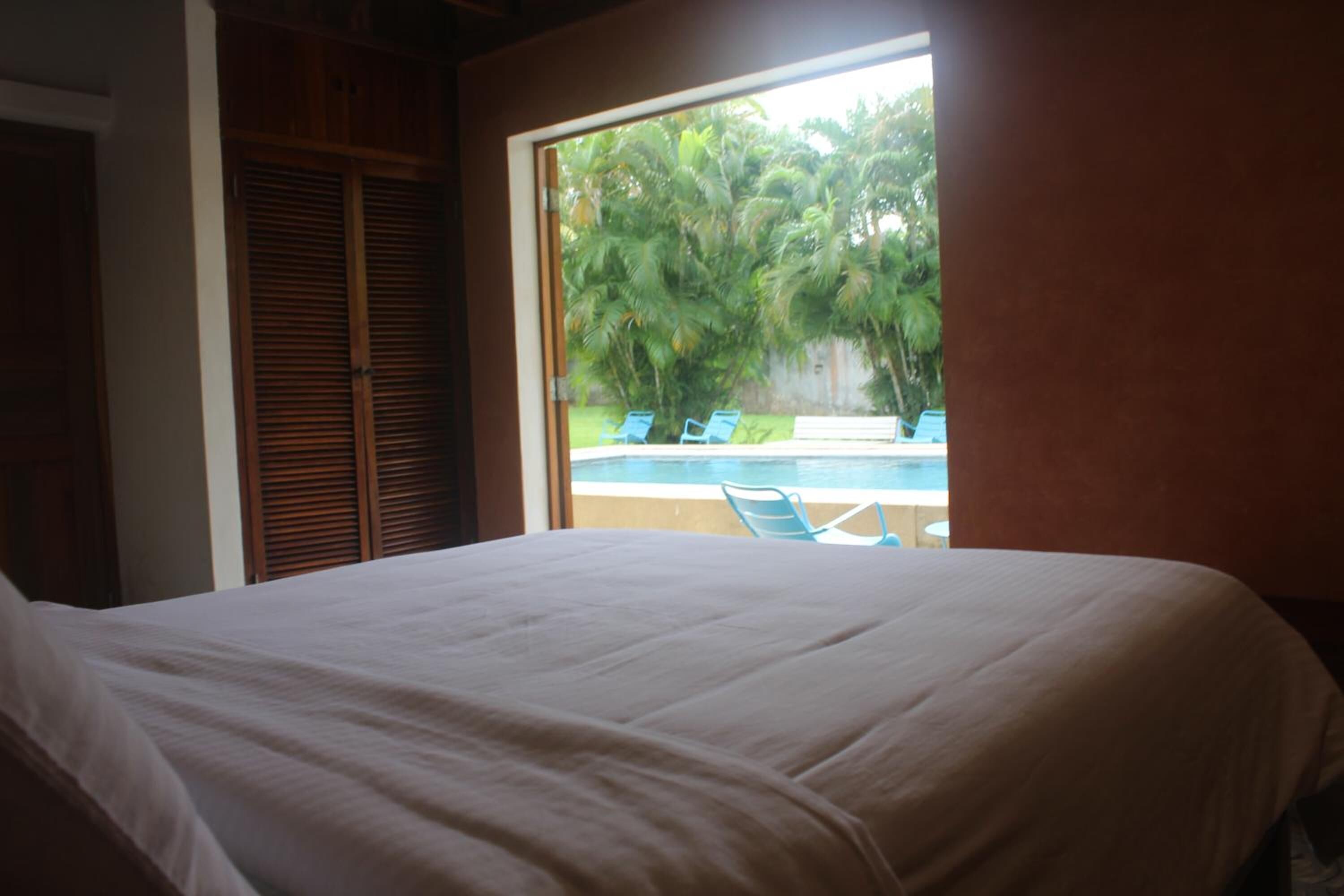 Un dormitorio con una cama grande, un armario de madera y vistas a una piscina y palmeras a través de una ventana.