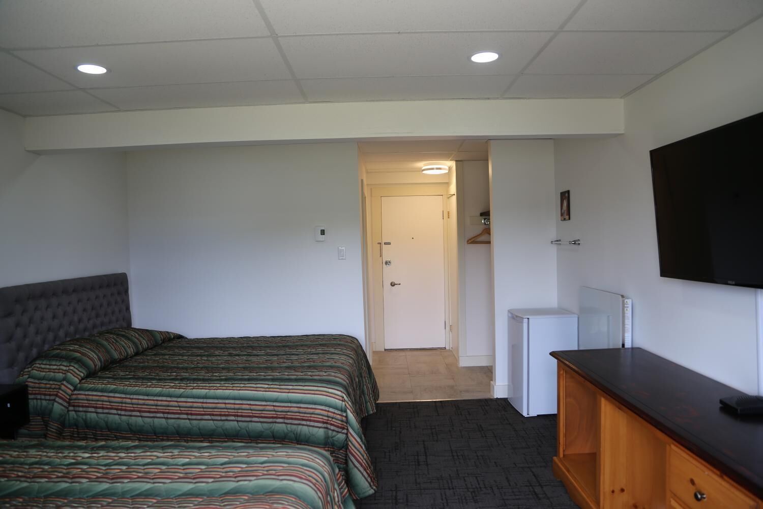 A hotel room with a bed, a TV, a dresser, and a door leading to a hallway.