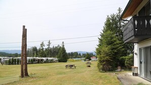 A grassy area with picnic tables, a wooden post, and RVs in the background. - Timberlodge RV & Campground (Port Alberni)
