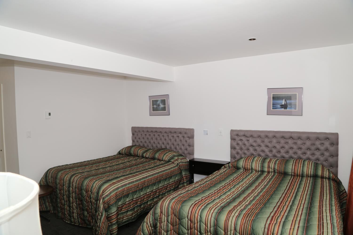 Une petite chambre propre, avec deux lits, chacun recouvert d’une couette à rayures, un mur blanc et une petite fenêtre.