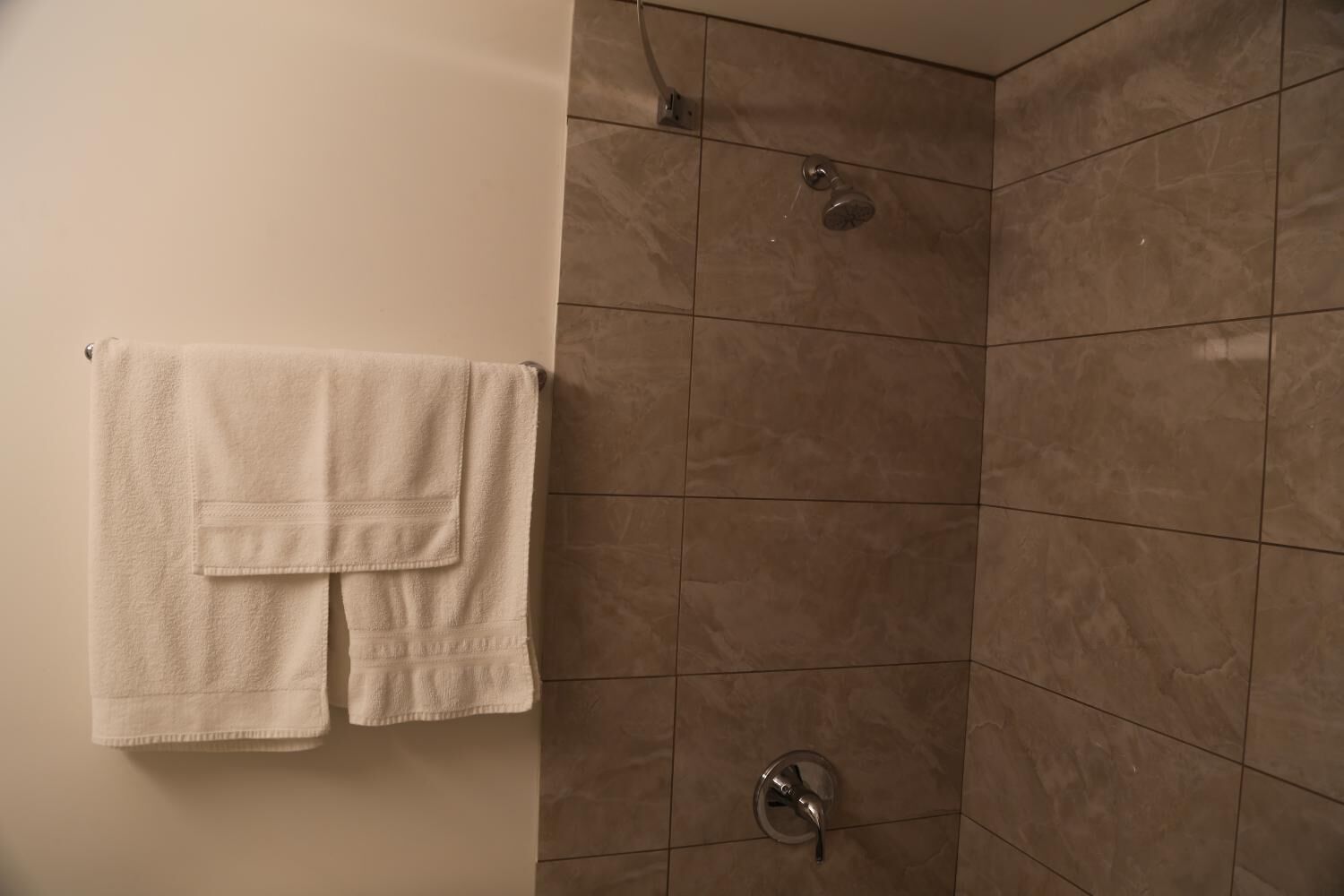 Un baño con ducha, paredes de azulejos y una toalla colgada en la pared.