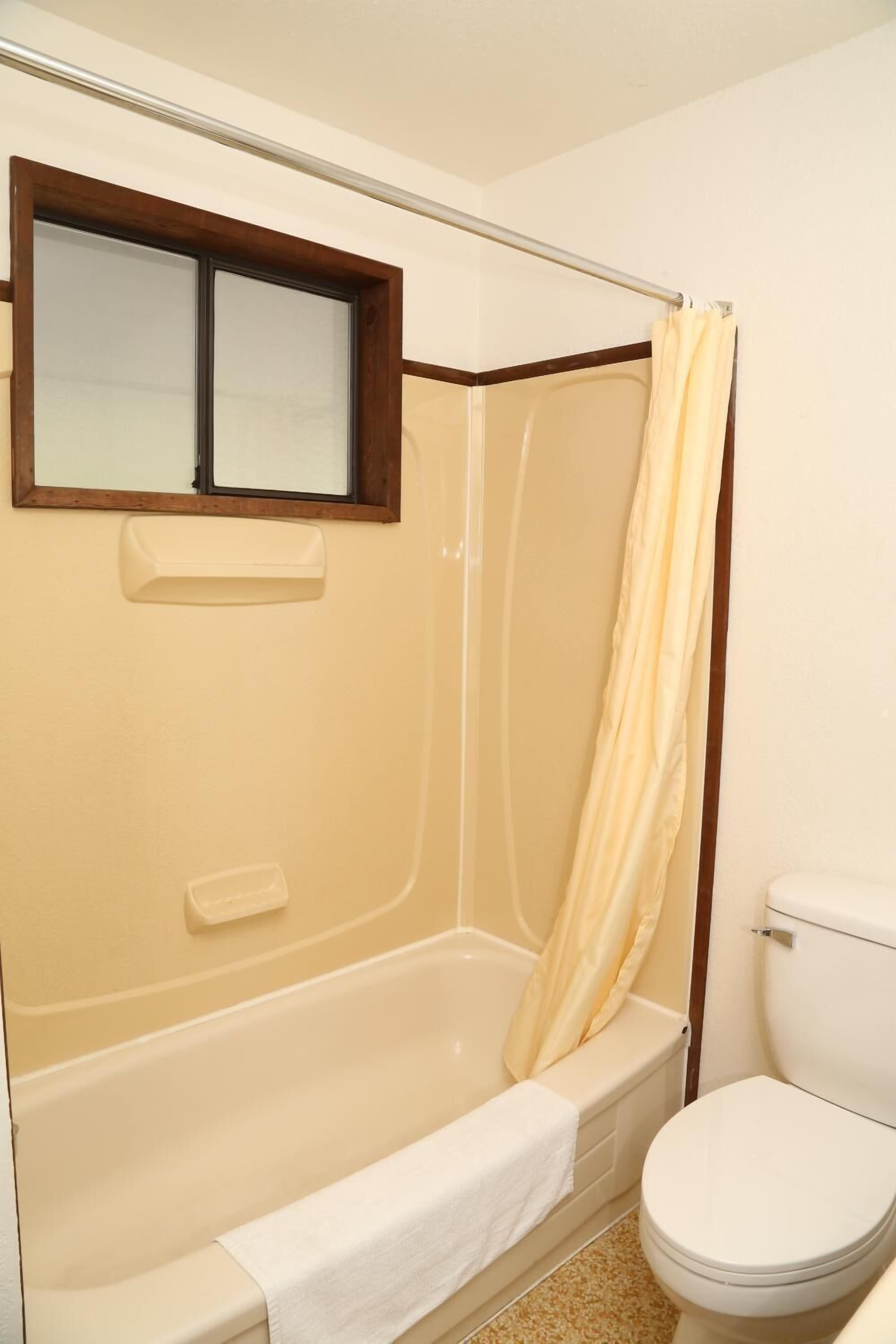 Ein Badezimmer mit einer Badewanne, einer Toilette und einem Fenster über der Wanne.
