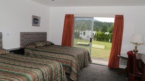 A hotel room with two beds, a sliding glass door to the outside, and a desk with a lamp. - Timberlodge RV & Campground (Port Alberni)