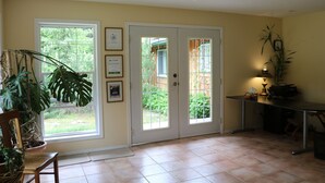 A room with a large window, a door, a chair, a table, and a potted plant. - Mulvehill Creek Wilderness Inn (Revelstoke)
