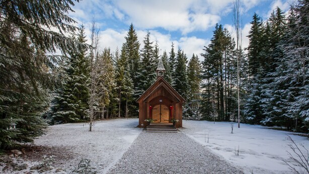A wooden cabin with a steep roof, surrounded by snow-covered trees and a gravel path leading to the entrance. - Mulvehill Creek Wilderness Inn (Revelstoke)