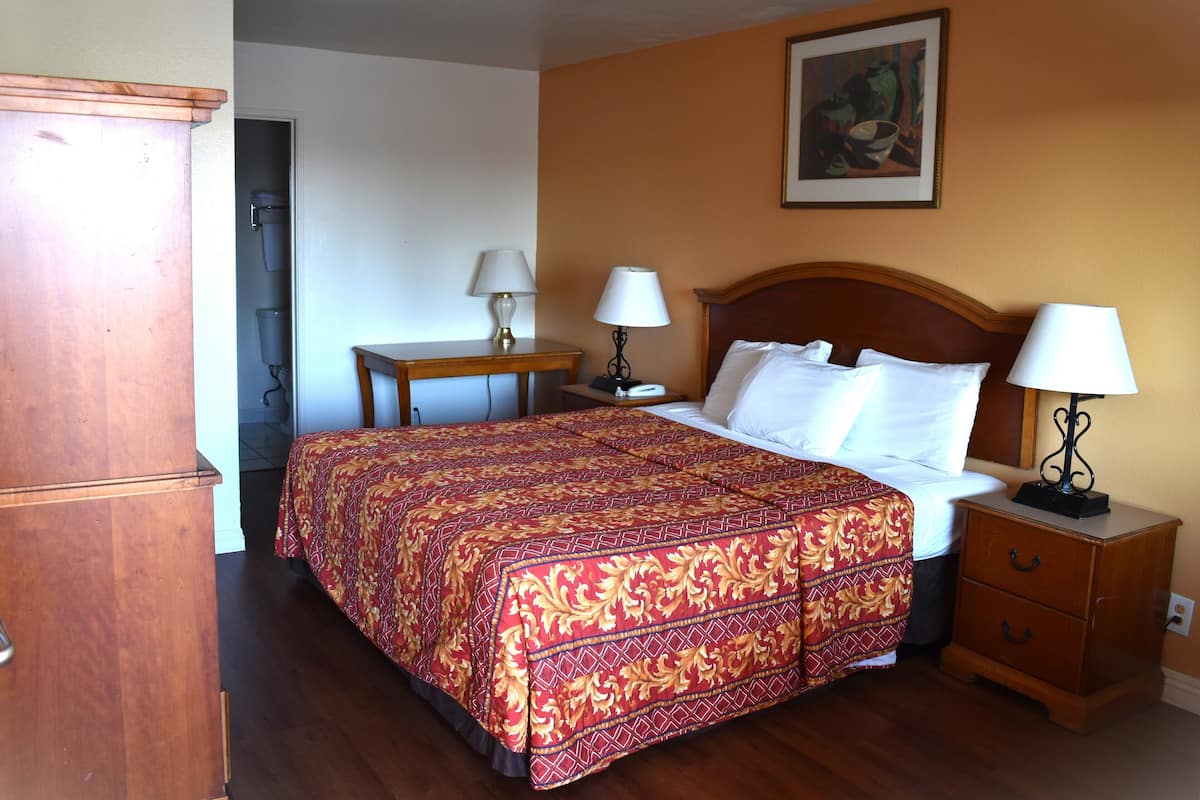 A hotel room with a bed, bedside tables, lamps, a wooden wardrobe, and a painting on the wall.