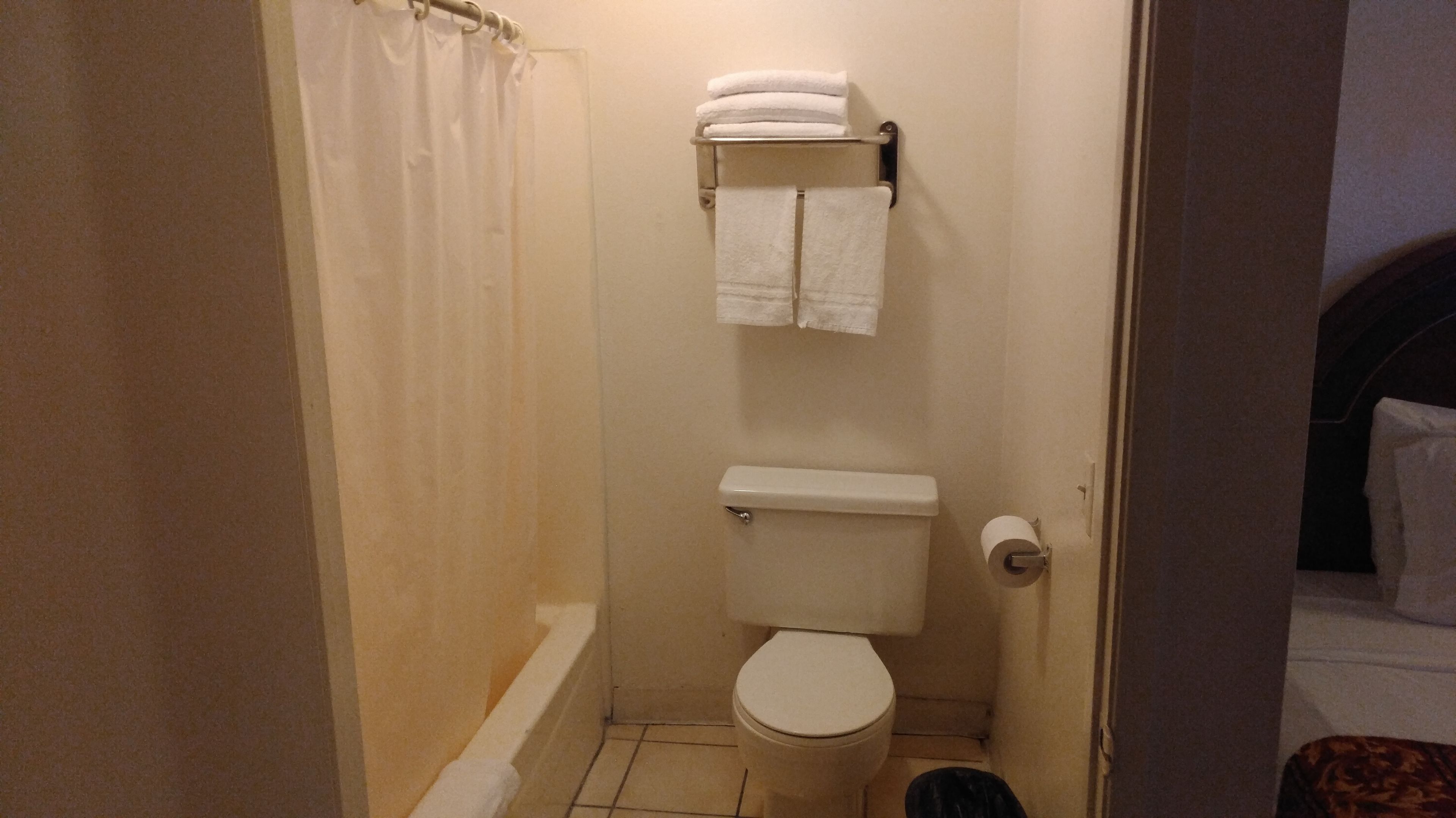A small, compact bathroom with a toilet, a towel rack with folded towels, and a shower curtain.