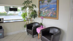 Una habitación con dos sillones de cuero, una mesita con mantel rosa, una planta en maceta y un cuadro de una escena costera.