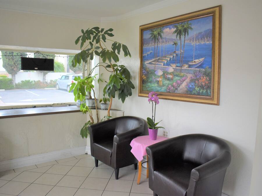 Una habitación con dos sillones de cuero, una mesita con mantel rosa, una planta en maceta y un cuadro de una escena costera.