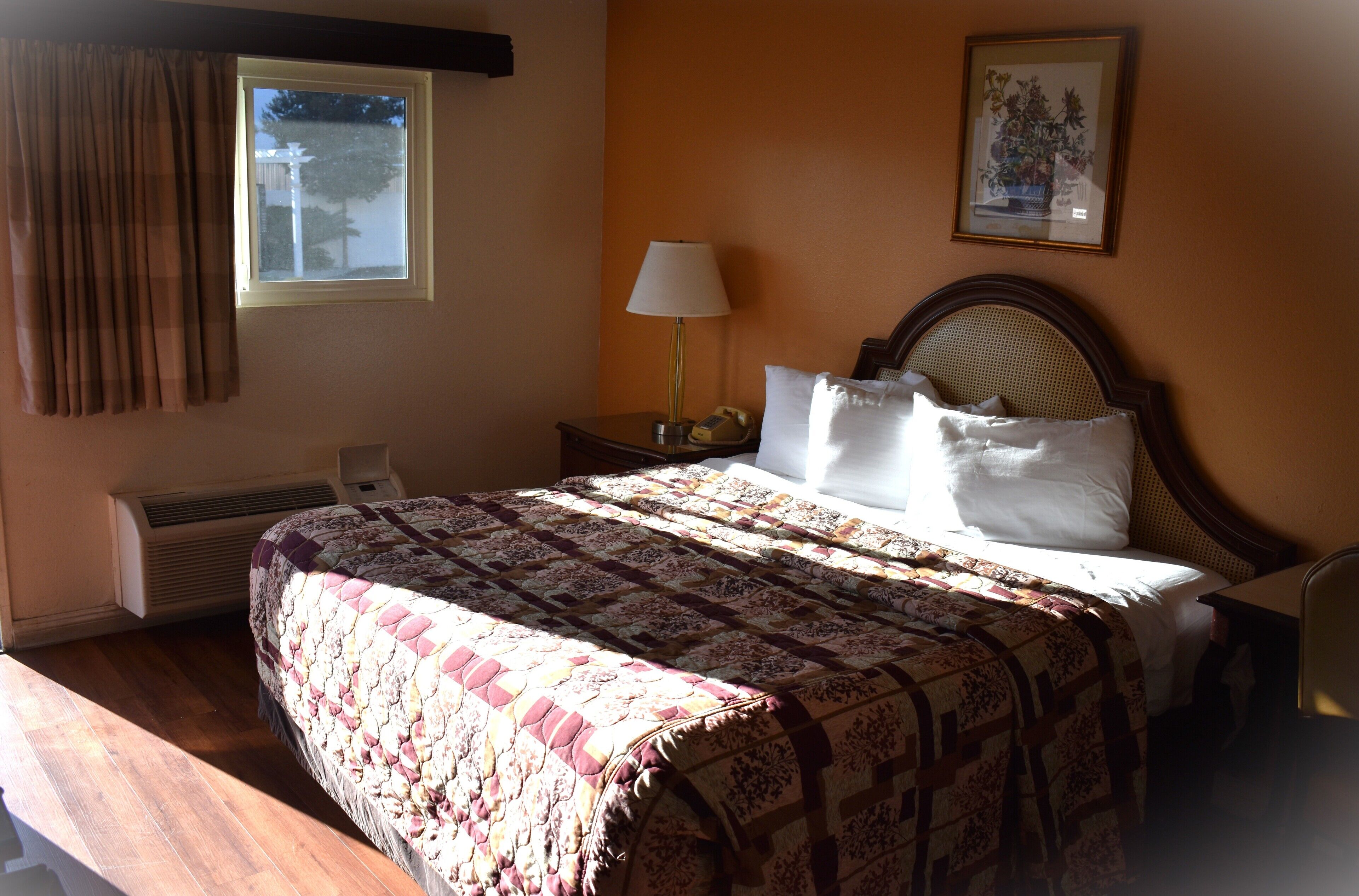 A neatly made bed with a patterned bedspread, a bedside lamp, and a framed picture on the wall.