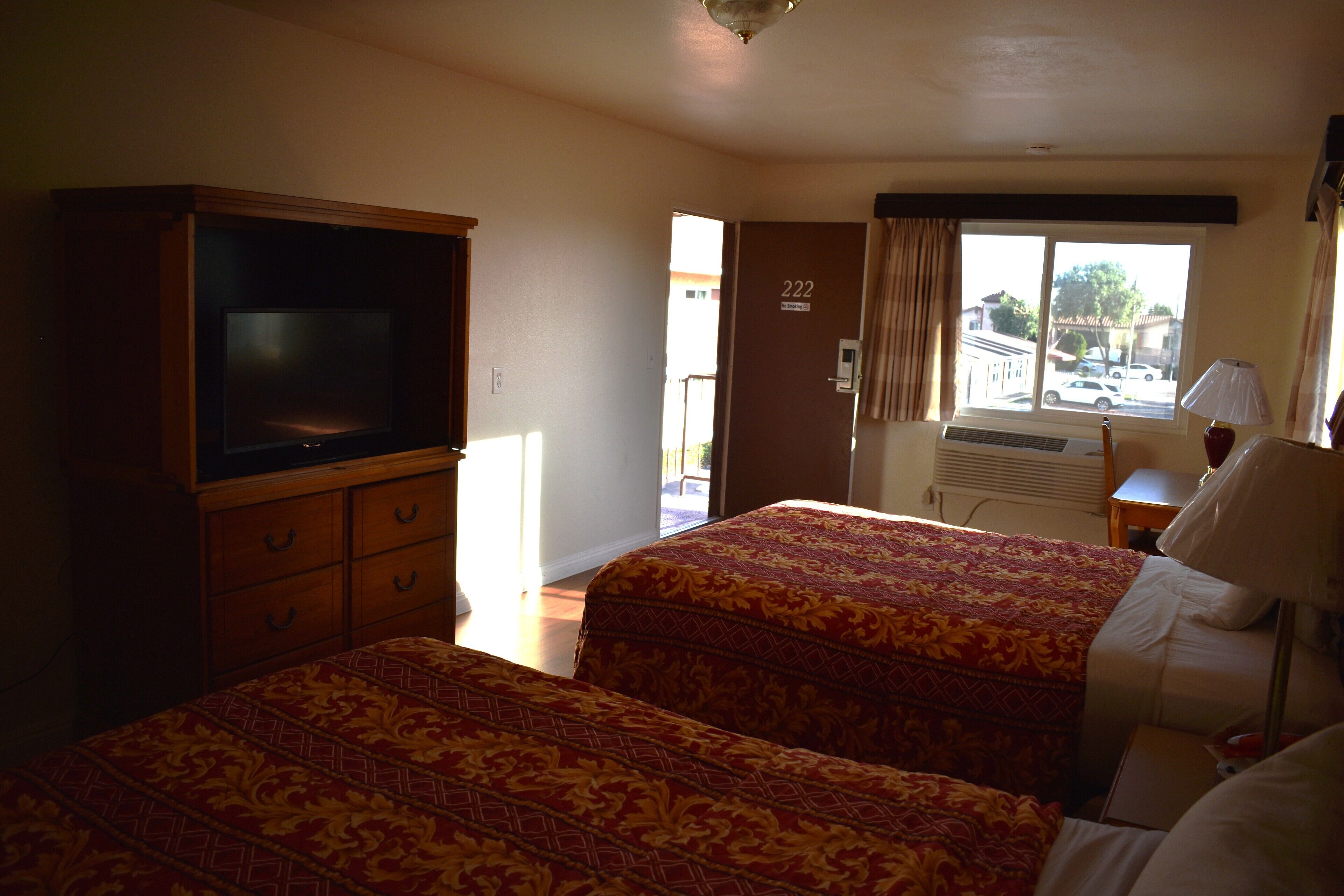A hotel room with two beds, a television, a desk, and a window with a view of the outside.