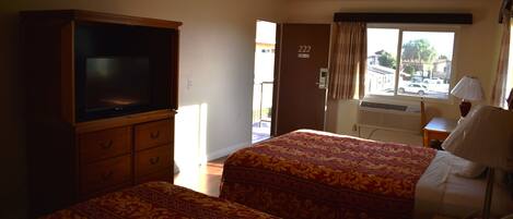 A hotel room with two beds, a television, a desk, and a window with a view of the outside.