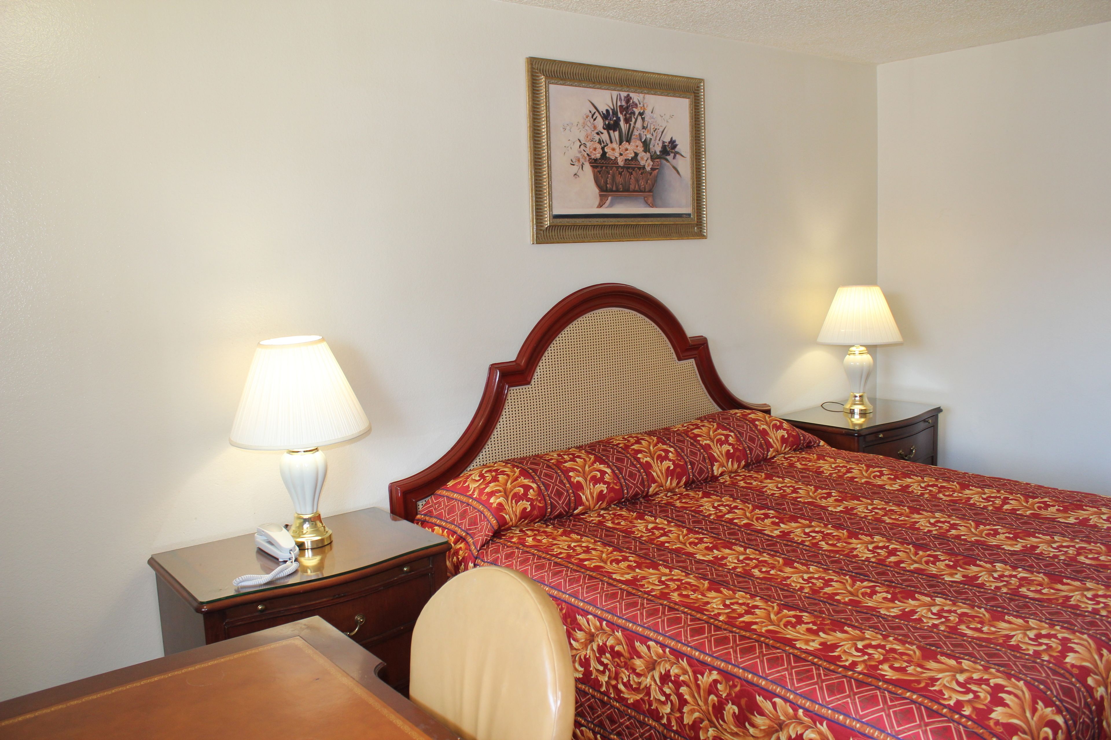 A hotel room with a bed, two bedside tables with lamps, a chair, a desk, and a framed picture on the wall.