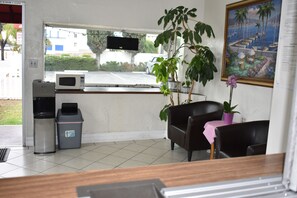 A small room with a window, a microwave, a trash bin, a potted plant, and a painting on the wall. - Valley Hotel (Rosemead)