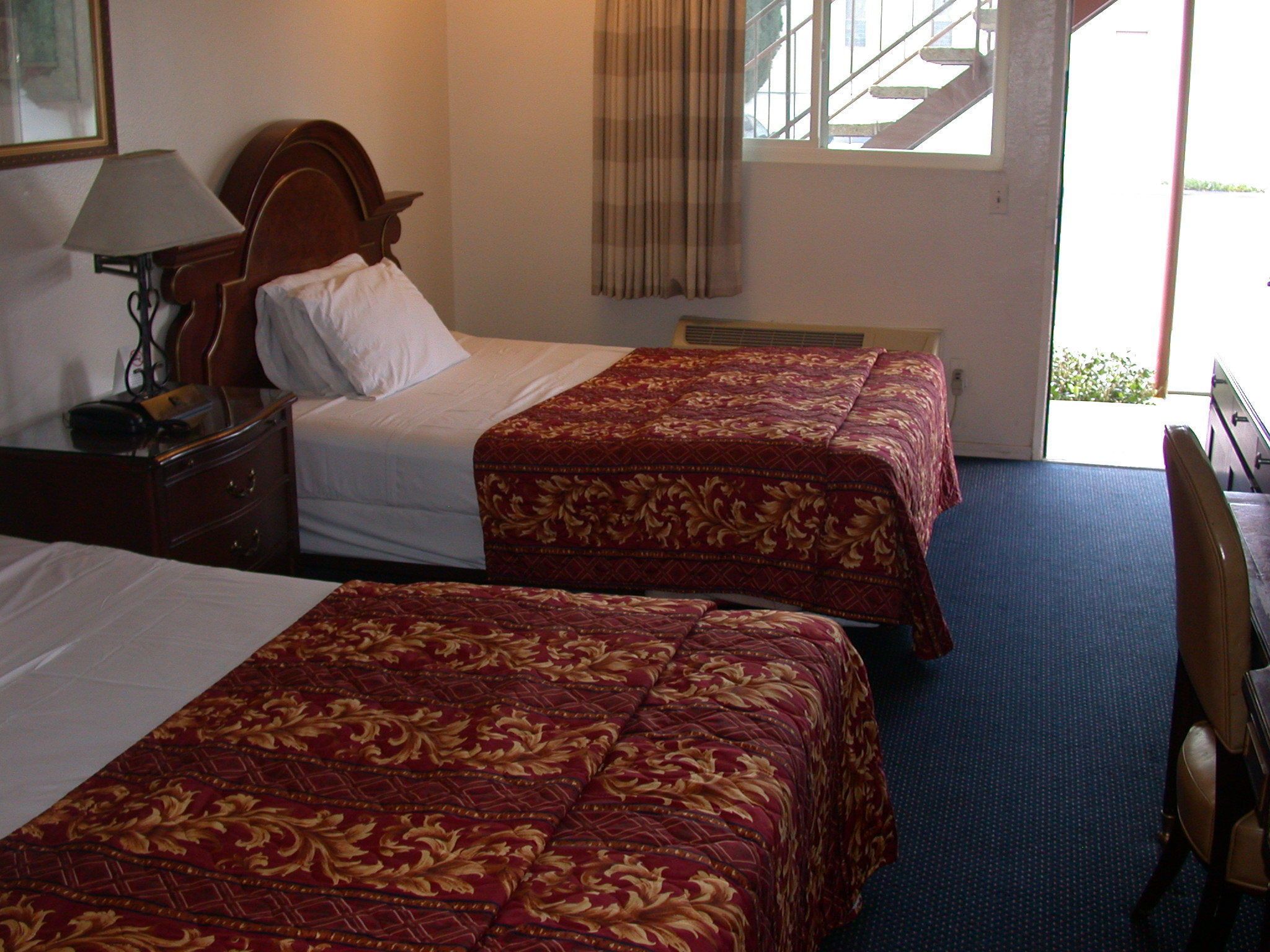 Habitación de hotel con dos camas, un escritorio, una lámpara y vistas al exterior.