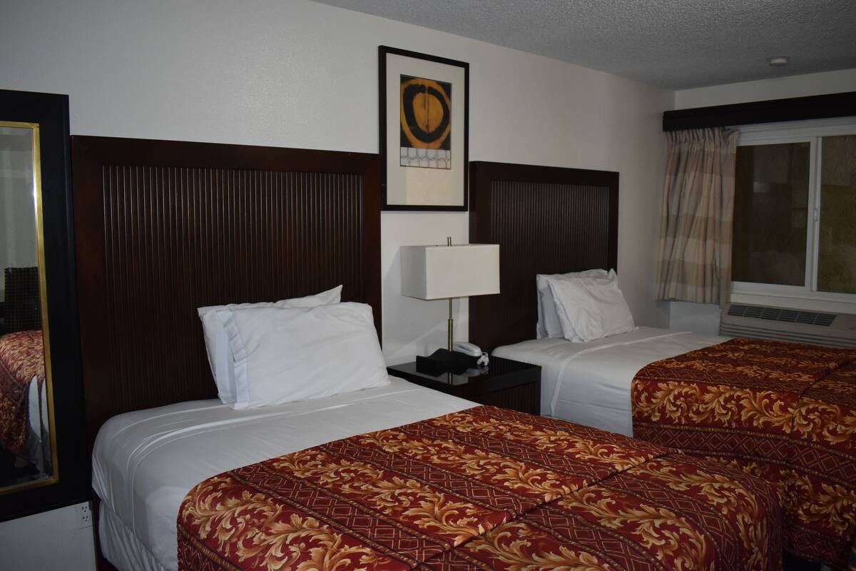 A hotel room with two beds, a nightstand, a lamp, and a framed picture on the wall.