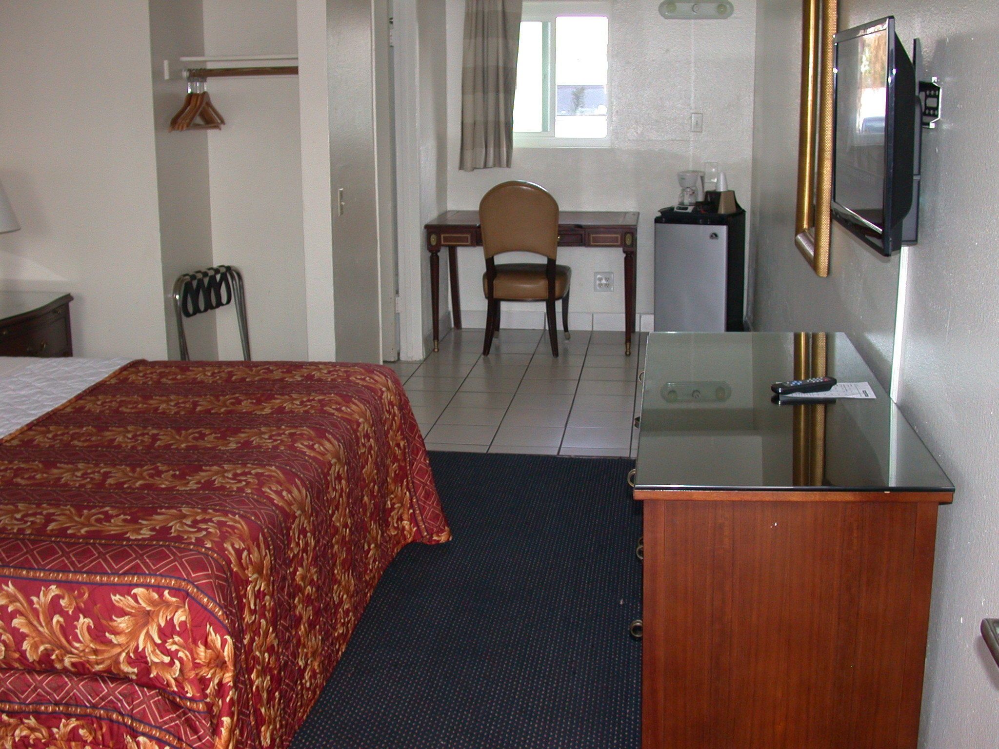 Una camera d'albergo con un letto, una scrivania, una sedia, un televisore e un piccolo frigorifero.