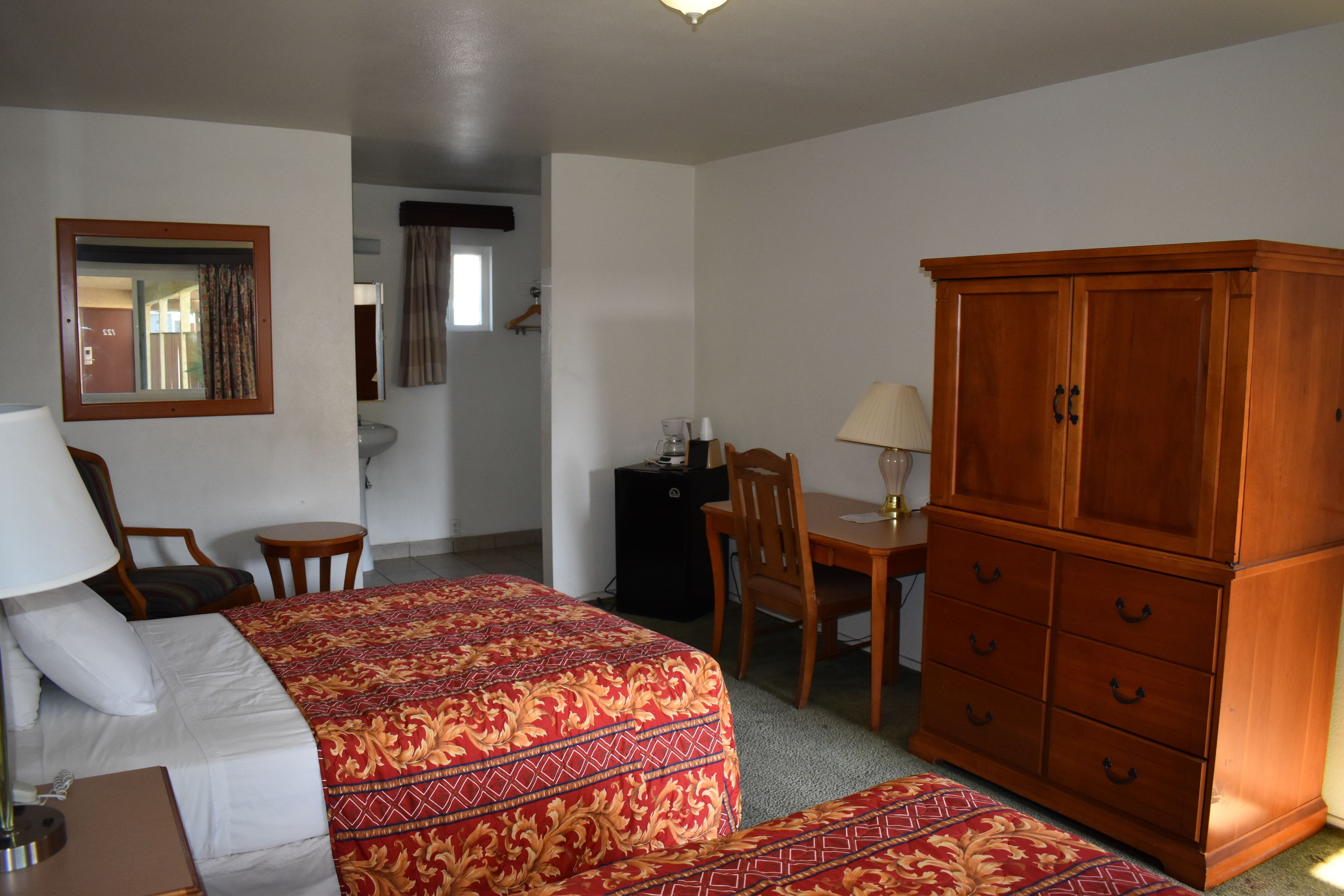 Une chambre d’hôtel comprenant un lit, un bureau, une chaise, une armoire et un miroir.