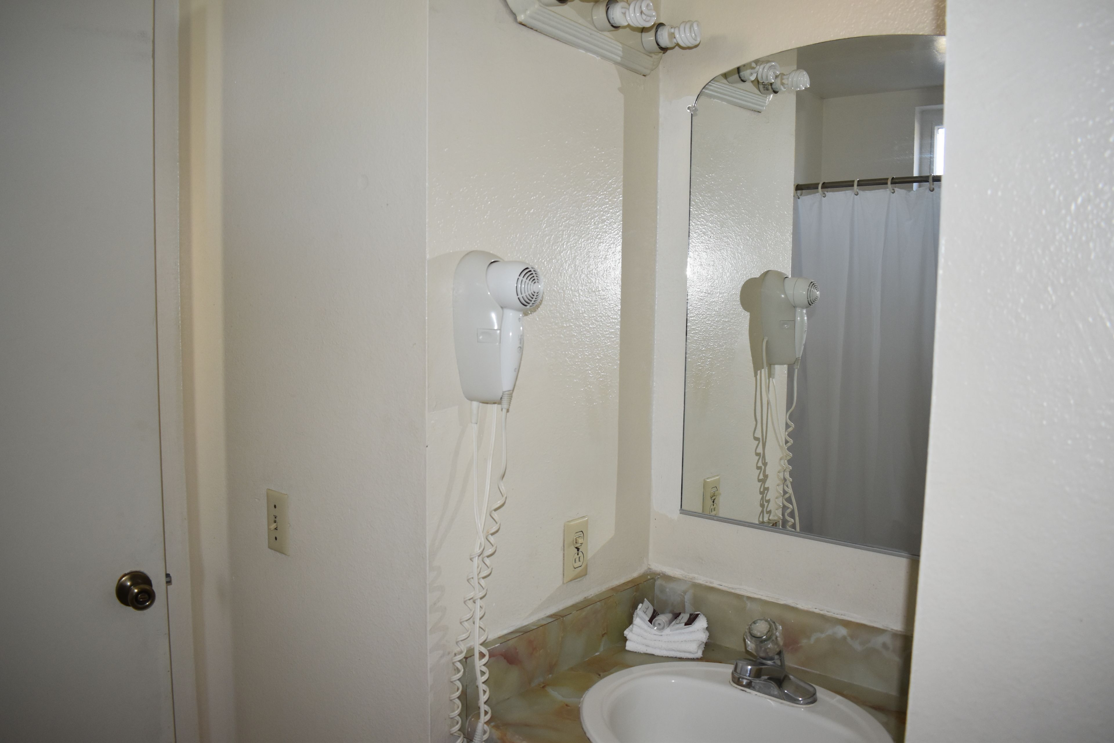 A bathroom with a white sink, a mirror, and a hairdryer mounted on the wall.