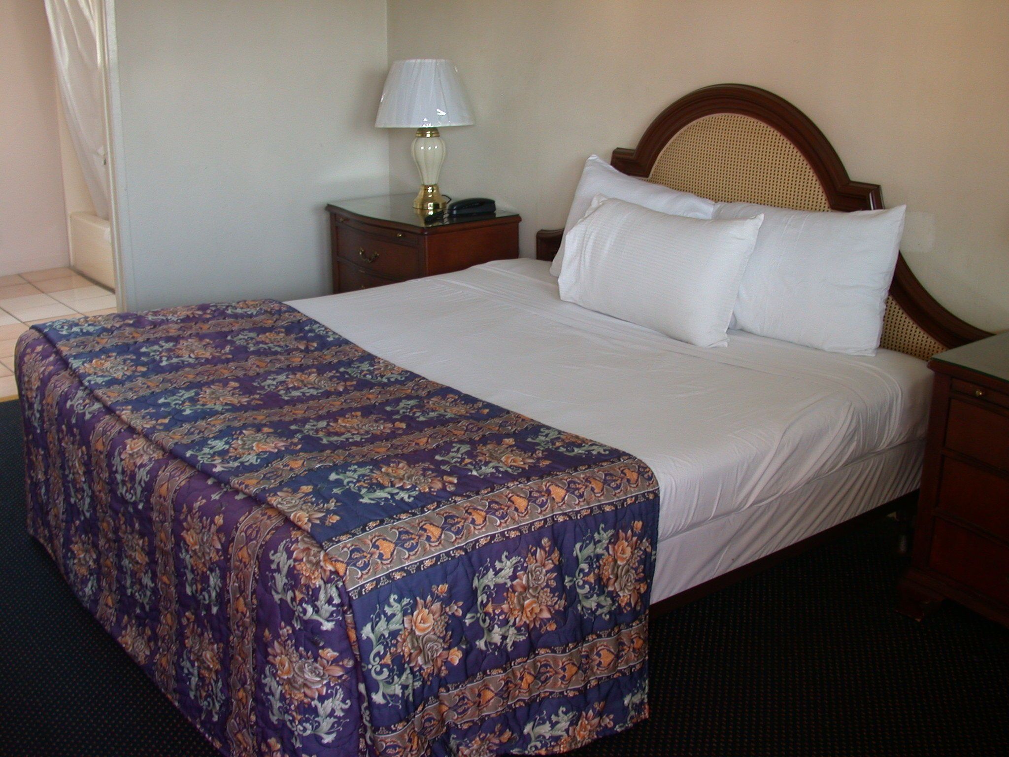 A neatly made bed with a floral bedspread, a wooden headboard, and a bedside lamp.
