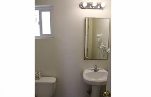 A bathroom with a toilet, a sink, a mirror, and a window. - Valley Hotel (Rosemead)