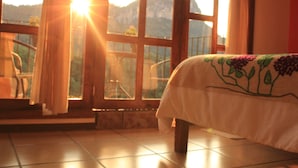 Una habitación con cama, ventana con cortinas y vistas a montañas.