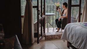 Un balcón con vistas a un área boscosa, una mesa pequeña con una planta en maceta y una cama con una colcha blanca.