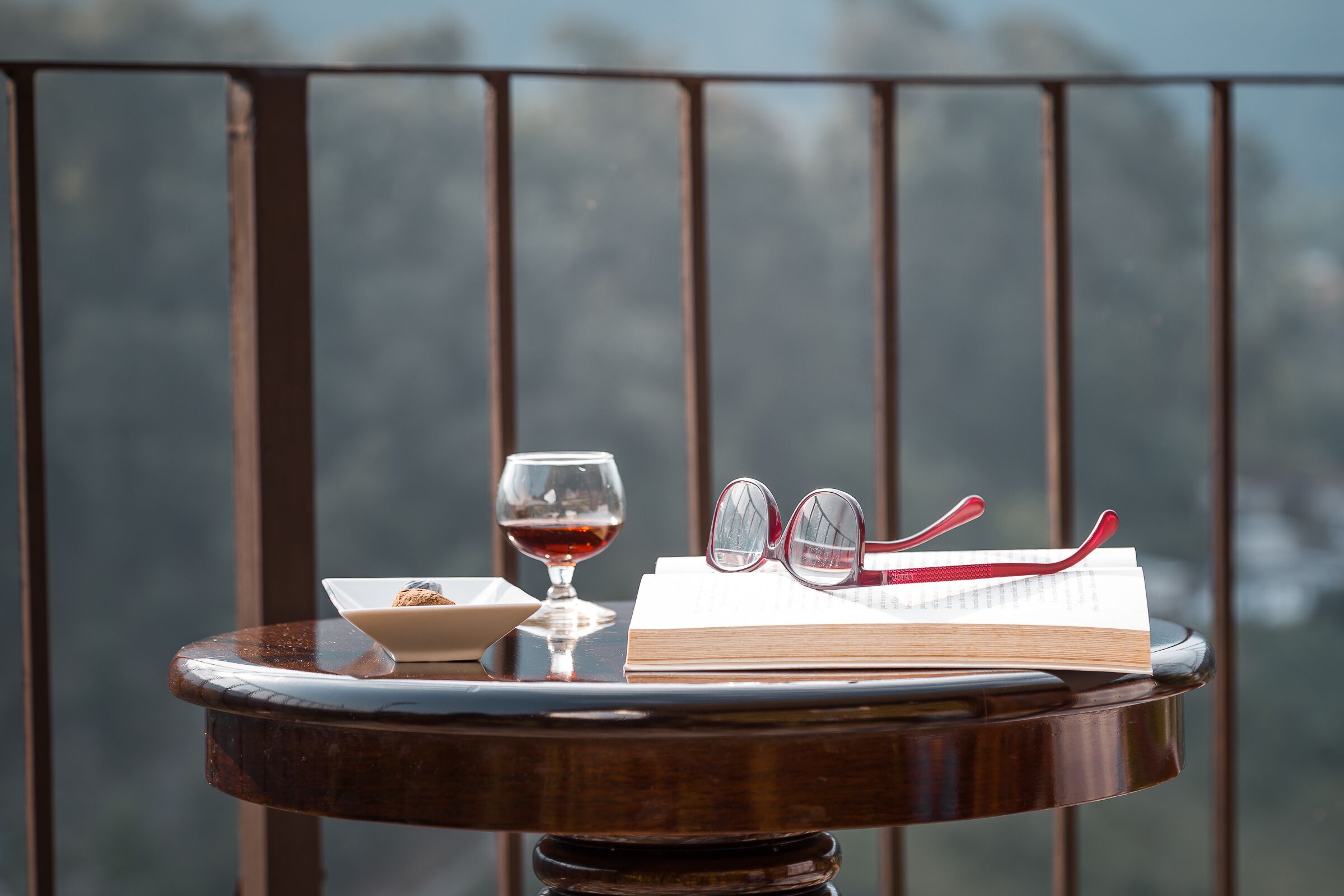 A round wooden table with a book, a wine glass, and a pair of glasses on it.
