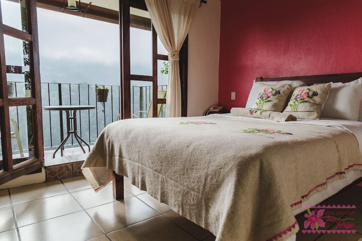 Ein Schlafzimmer mit einem Bett, einem kleinen Tisch und einem Stuhl neben einem Balkon mit Blick.