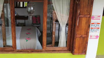 Una habitación con cama, ventana con cortinas, puerta de madera y una pared con un cartel.