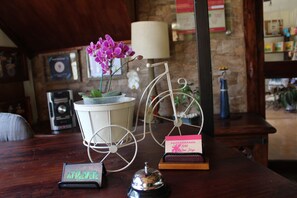 A wooden table with a white metal stand holding a pink card, a small black bell, and a green card.