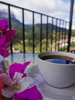 A cup of coffee on a table with a mountain view.
