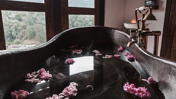 Una bañera con pétalos de rosa flotando en el agua, un grifo de bronce y vistas a las montañas a través de amplios ventanales.