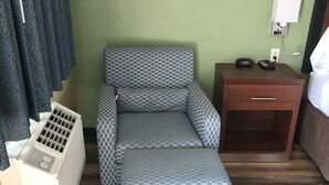 A hotel room with a bed, a bedside table with a lamp, a heater, and a patterned sofa. - Knight's Inn Motel (Grants Pass)