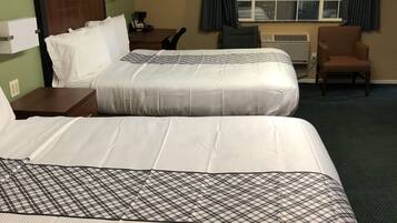 Habitación de hotel con dos camas, un escritorio, una silla, un ventanal con cortinas y un equipo de aire acondicionado.