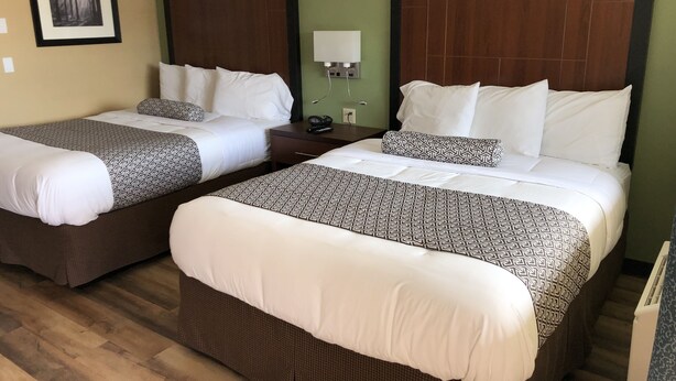 A hotel room with two beds, each with a patterned bedspread and white pillows. There is a nightstand with a lamp and a phone between the beds. - Knight's Inn Motel (Grants Pass)
