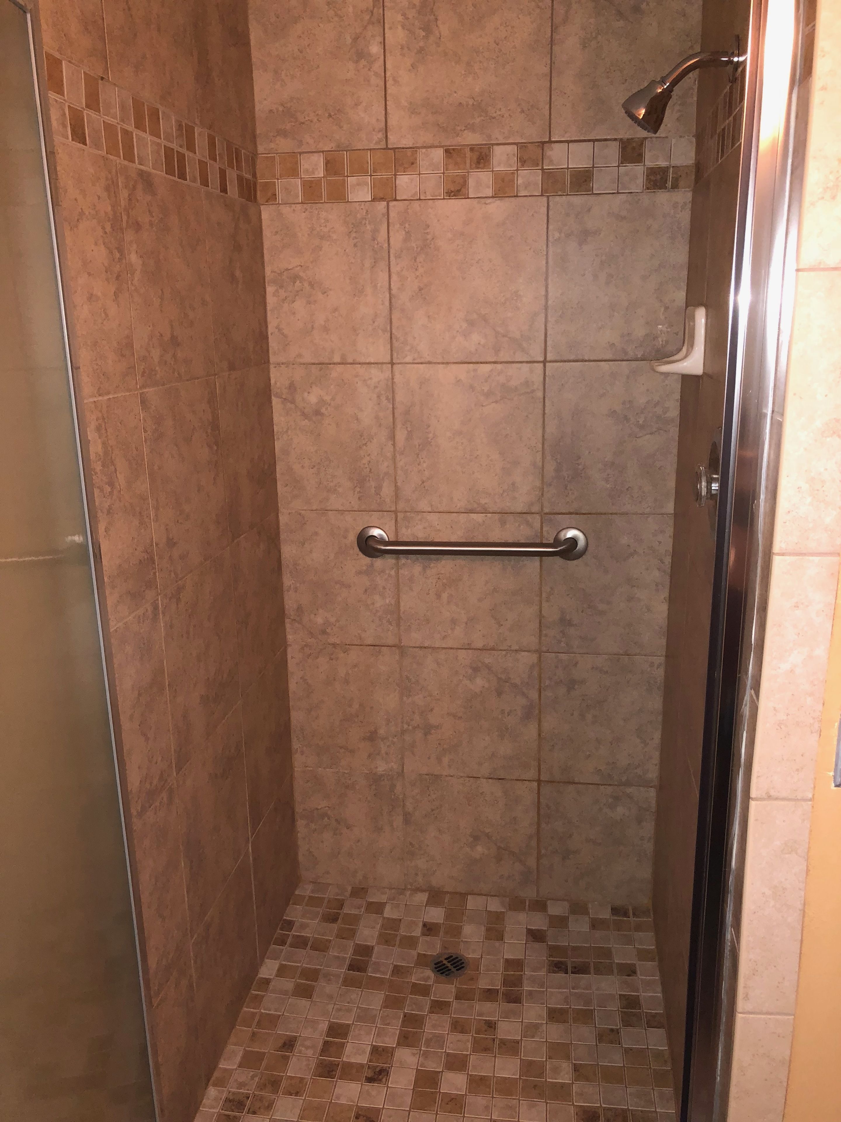Une douche à l’italienne avec une barre d’appui, des murs carrelés et un sol à motifs à carreaux.