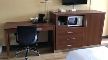 Et hotelværelse med et træskrivebord, en sort kontorstol, en seng med hvide sengetøj, et fladskærms-tv, en mikrobølgeovn og en telefon.