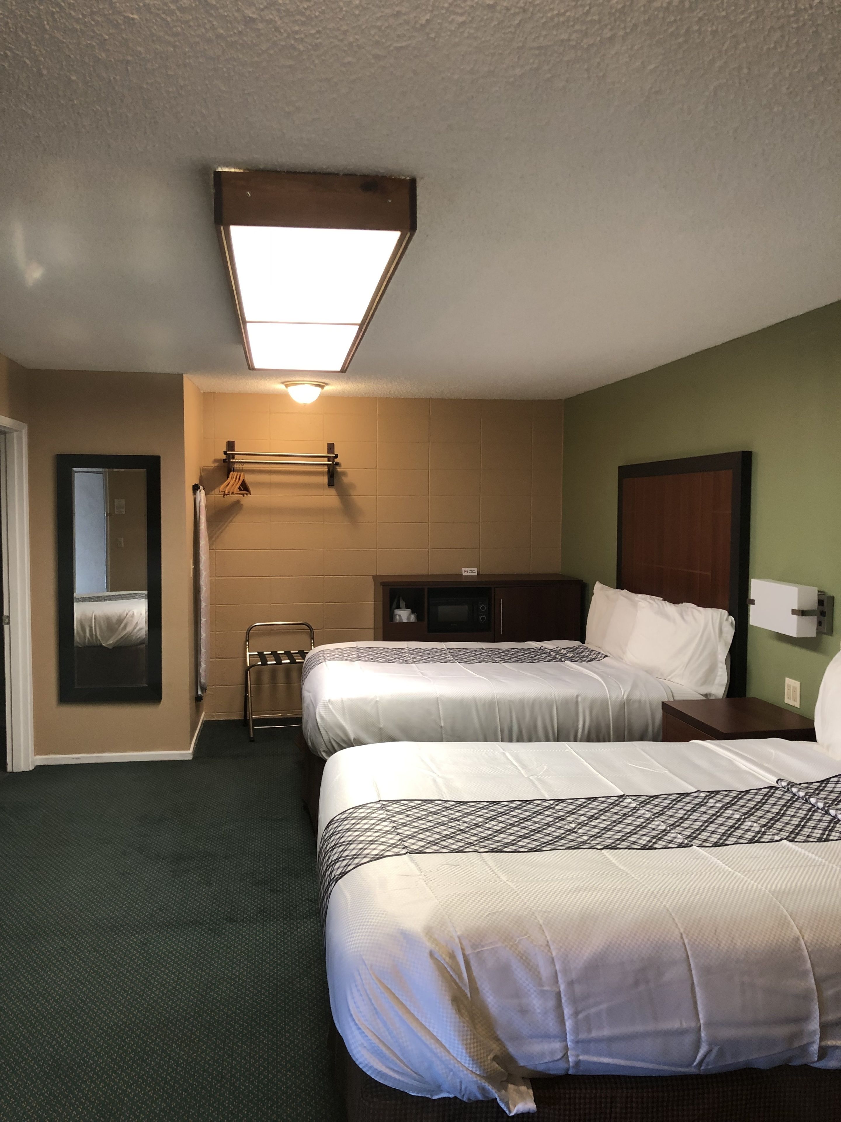 Habitación de hotel con dos camas, un espejo, un mueble bajo y una lámpara en el techo.