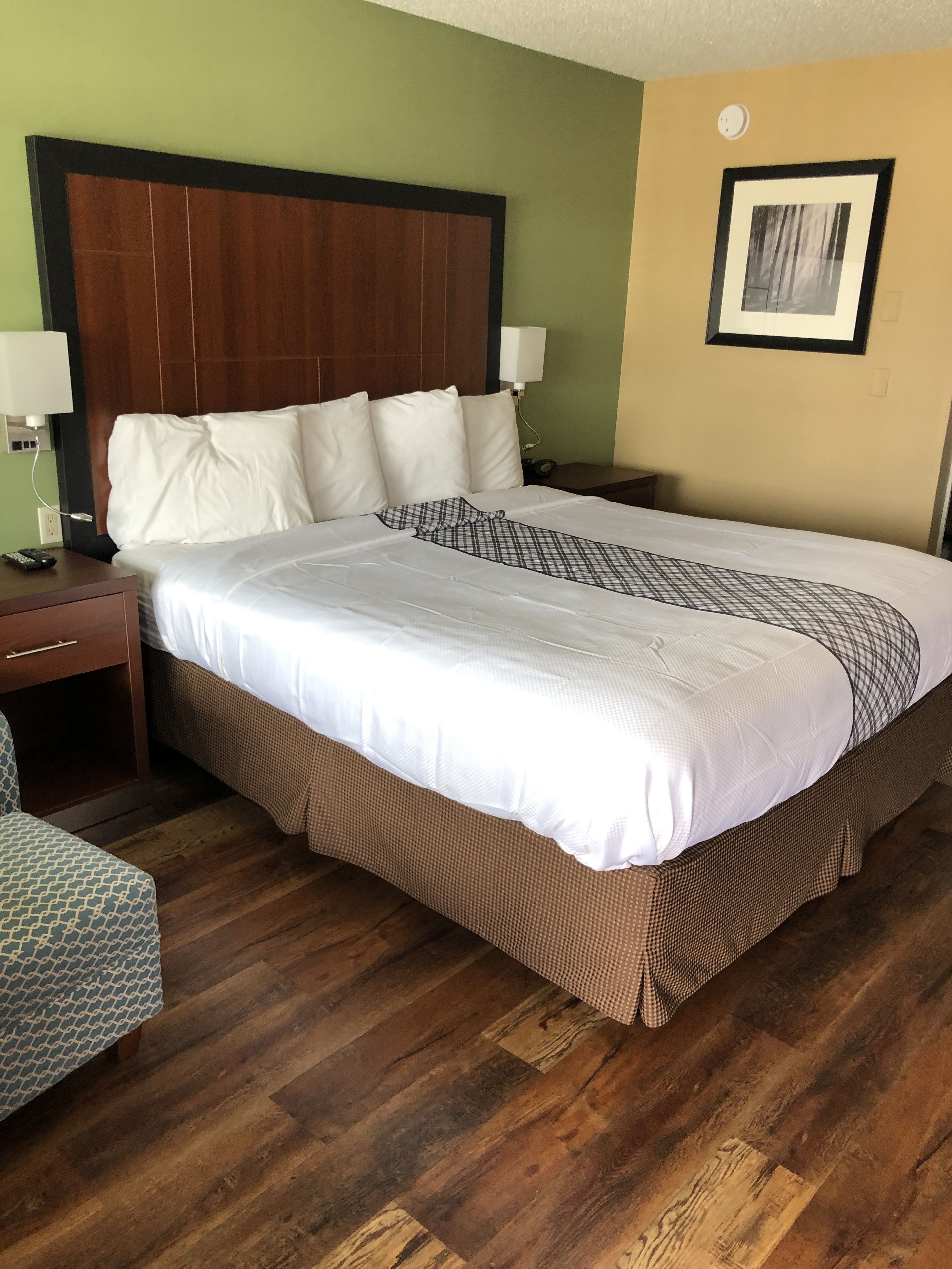 A hotel room with a large bed, two bedside tables, a nightstand, a chair, and a framed picture on the wall.