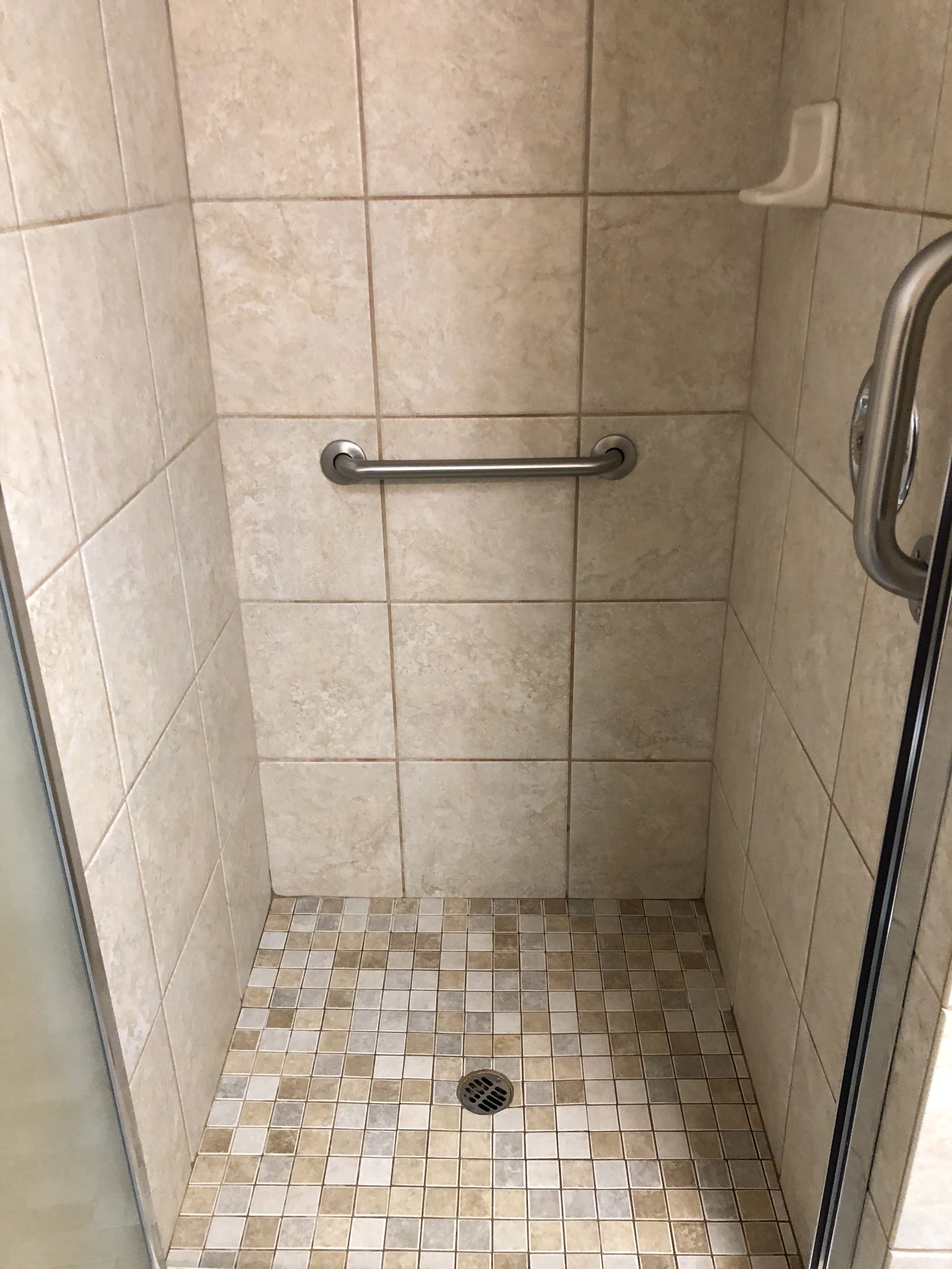 A small, tiled shower area with a grab bar and a drain.