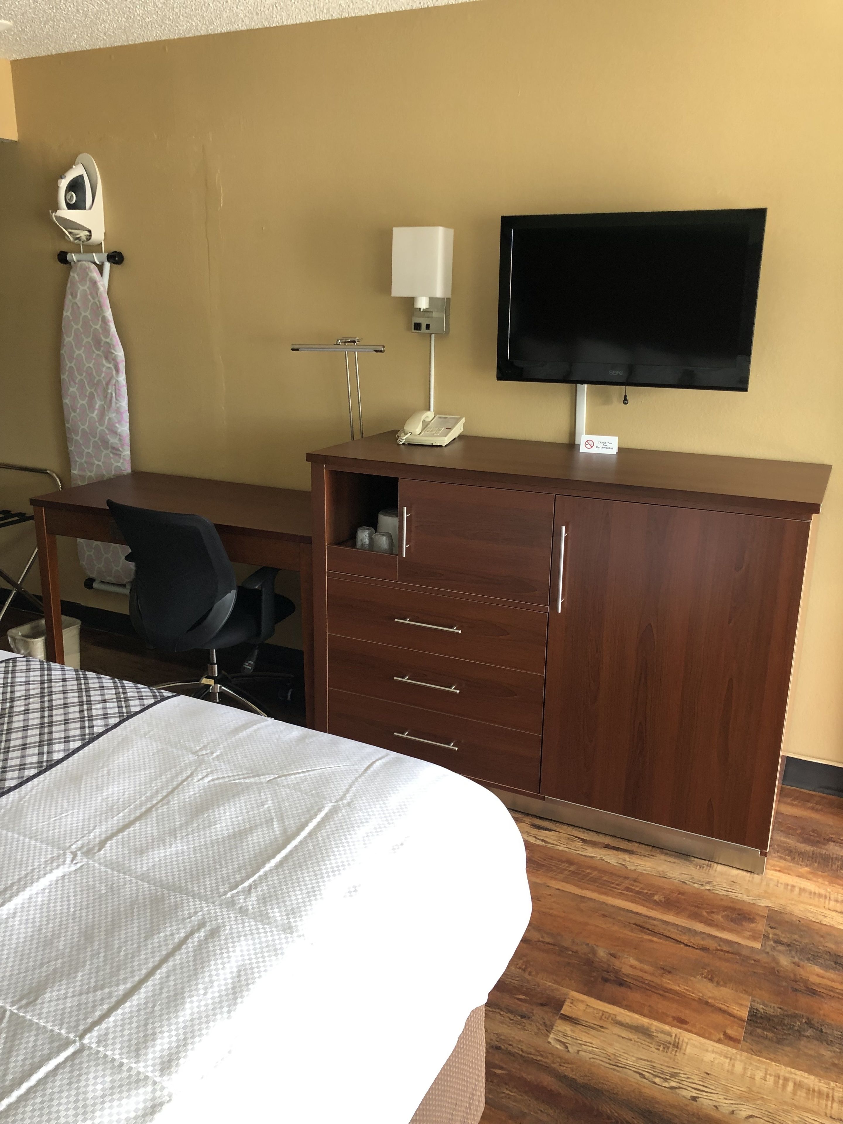 A hotel room with a bed, a desk with a chair, a television, a telephone, and a cabinet.