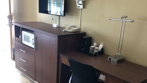 A hotel room with a wooden desk, a black office chair, a flat-screen TV mounted on the wall, a telephone, a coffee machine, and a lamp. - Knight's Inn Motel (Grants Pass)